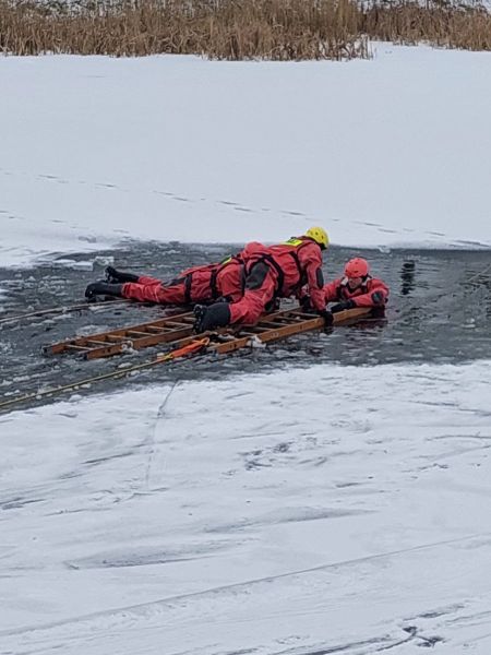 W trakcie ćwiczeń strażacy wykonują akcję ratunkową na zamarzniętym akwenie, udzielając pomocy w sytuacji zagrożenia.