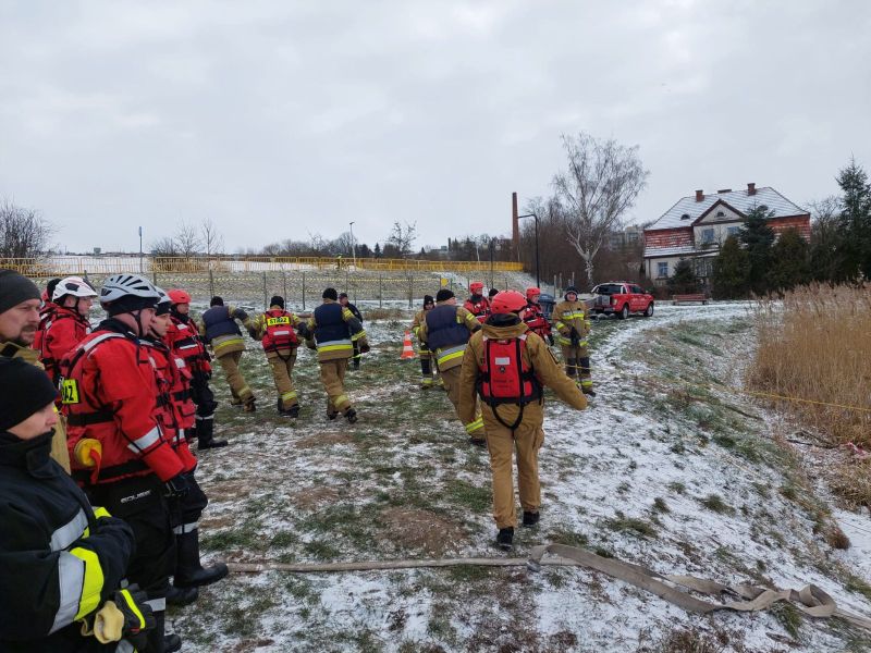 Strażacy w oczekiwaniu na swoją kolej obserwują kolegów, którzy biorą udział w ćwiczeniach ratunkowych na zamrożonym akwenie.