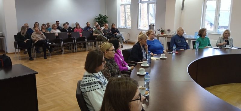 Druga grupa osób uczestnicząca w szkoleniu na miejscach siedzących przy okrągłym stole konferencyjnym oraz w tylnej części sali