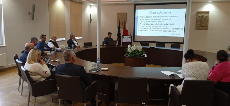 Trzecia grupa szkoleniowa uczestnicząca w szkoleniu na miejscach siedzących przy okrągłym stole konferencyjnym wraz z osobą prowadzącą szkolenie omawiającą program szkolenia