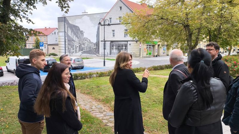 zdjęcie przestawia osoby stojące na tle muralu w Kwidzynie. 