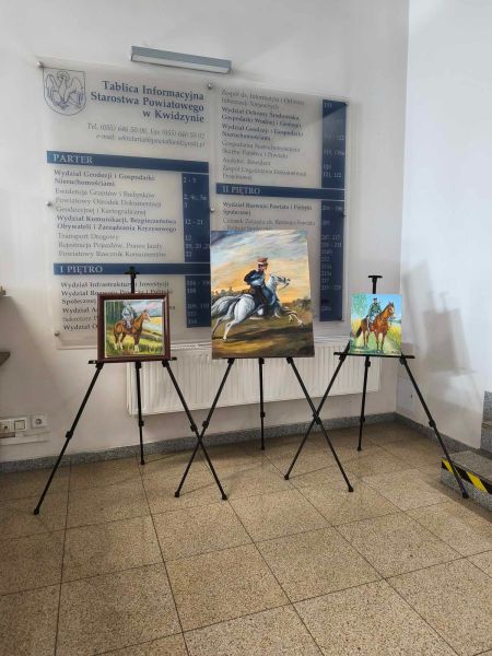 zdjęcie przedstawia trzy prace malarskie, na tle tablicy informacyjnej, na których widnieją mężczyźni jadący konno. 